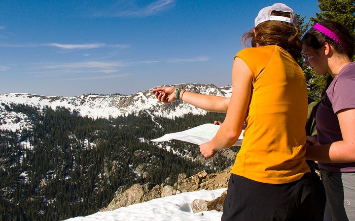 Two people stand on an overlook holding a map while one points